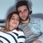 Man watching TV with headphones next to woman.