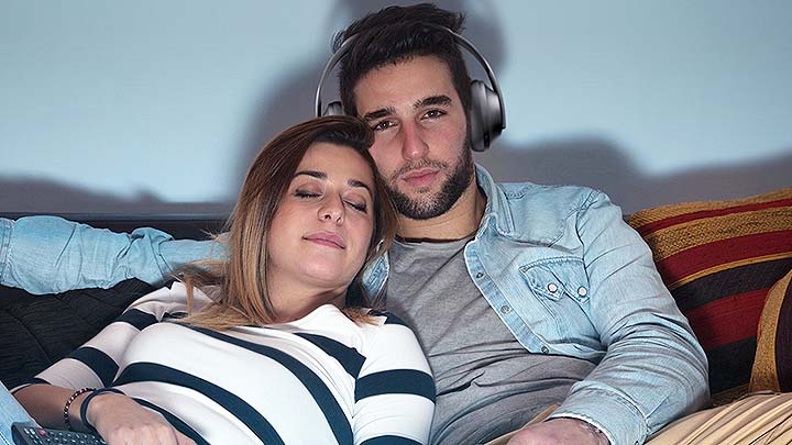 Man watching TV with headphones next to woman.