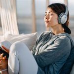 Woman sitting on couch wearing headphones and holding phone