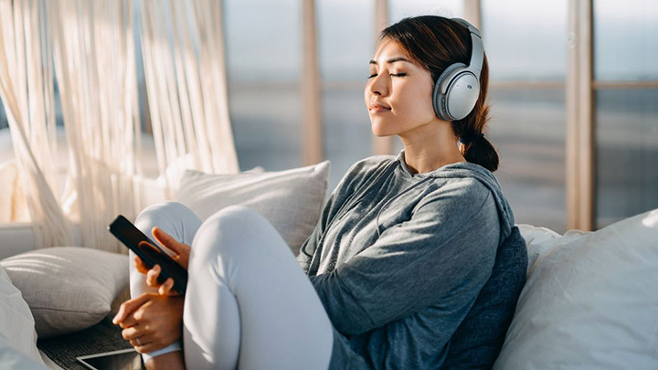 Woman sitting on couch wearing headphones and holding phone
